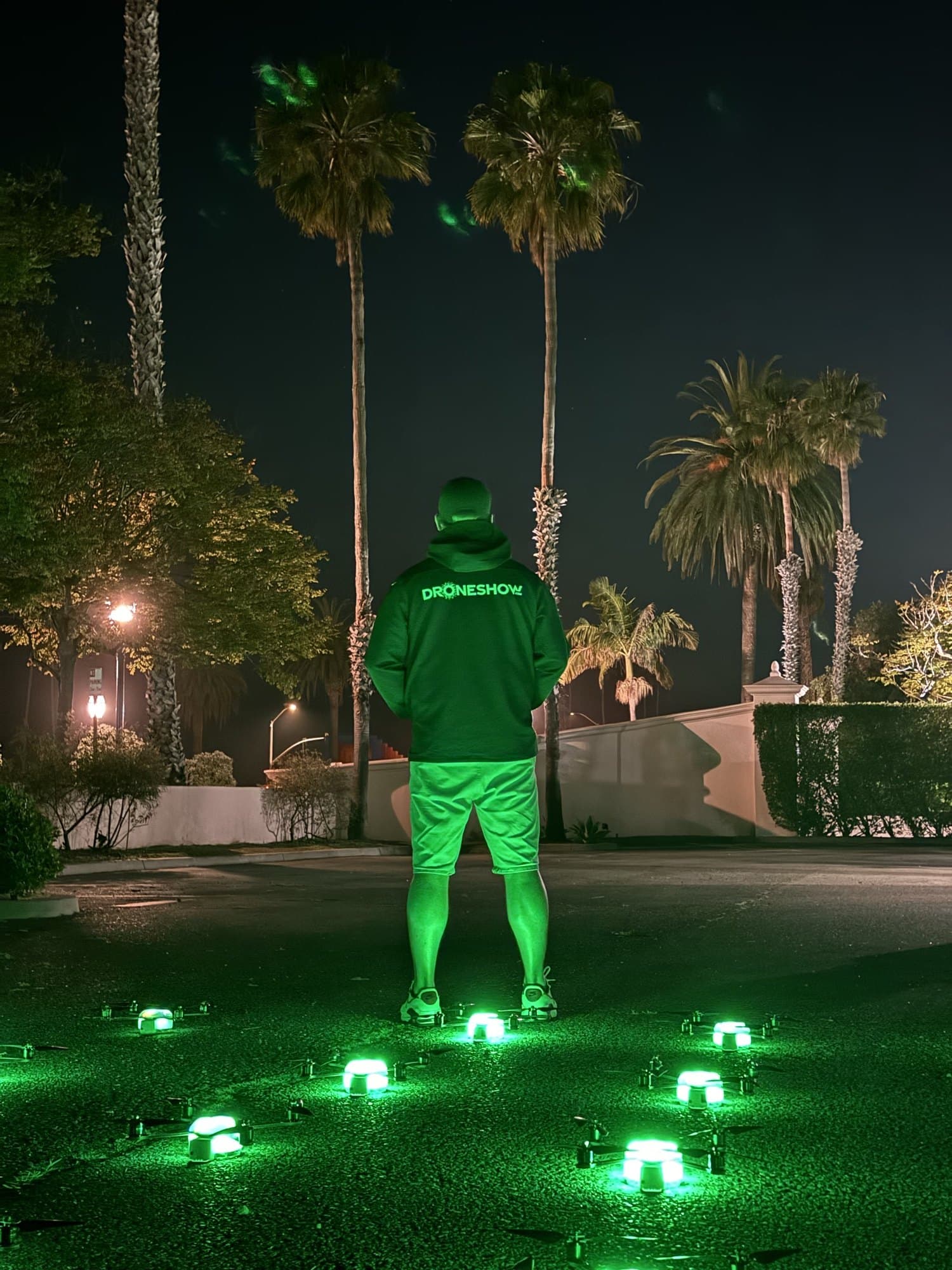 A pilot in a Droneshow hoodie standing over the launch grid, the aircraft lit green at their feet